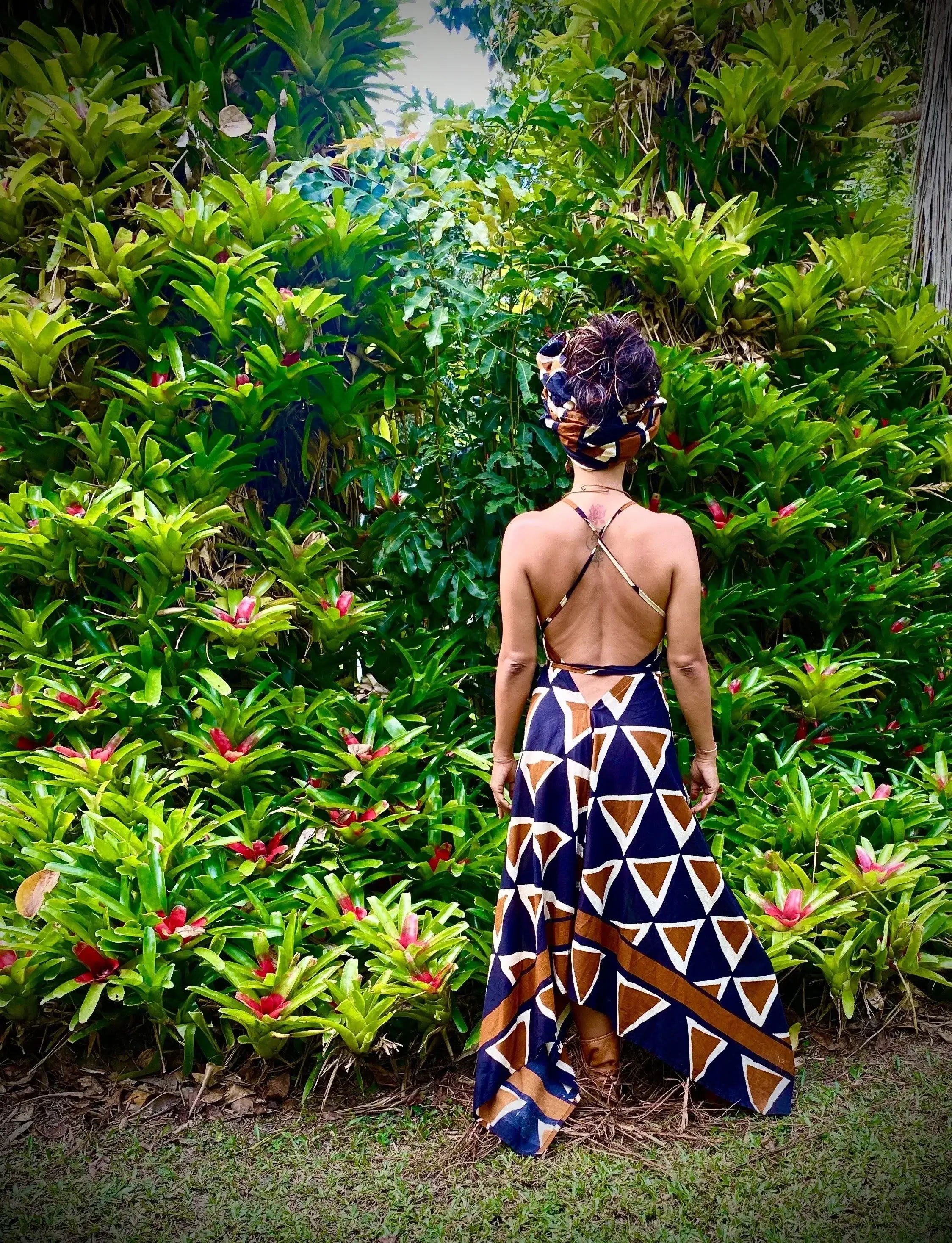 A woman wearing a stylish backless dress with geometric patterns, surrounded by lush greenery in a tropical setting, showcasing Ladies Dresses.