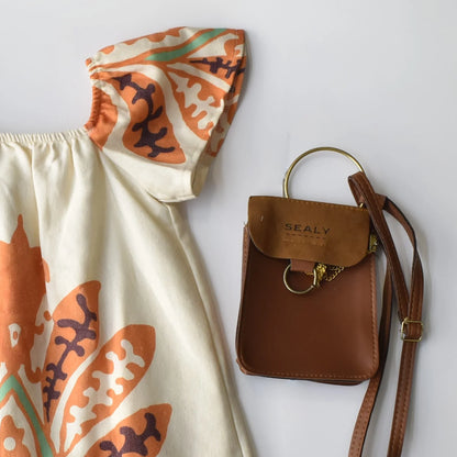 Tropical Isla Girls Linen Dress with floral print and puffed sleeves paired with a stylish brown crossbody bag.
