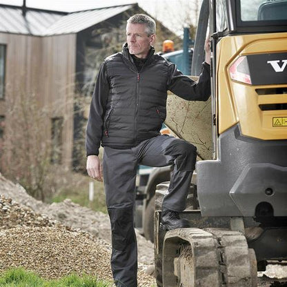 Mens Tuffstuff Excel Work Trousers - 710 worn by a man beside a construction vehicle, showcasing durability and style.