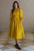 Freya Smocked Linen Midi Dress in yellow with puff sleeves and smocked bodice, set in a stylish indoor setting.