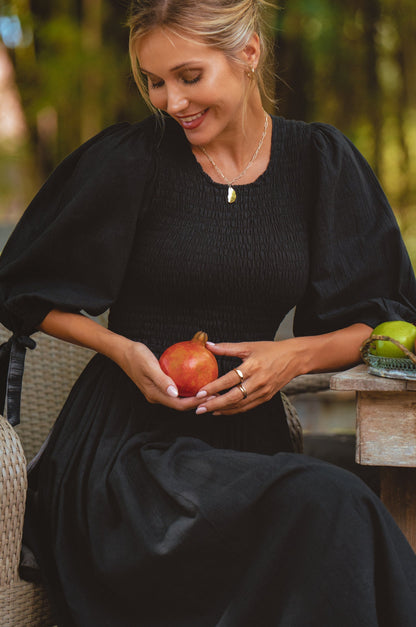 Freya Smocked Linen Midi Dress worn by a woman holding a pomegranate, showcasing its smocked bodice and puffy sleeves.