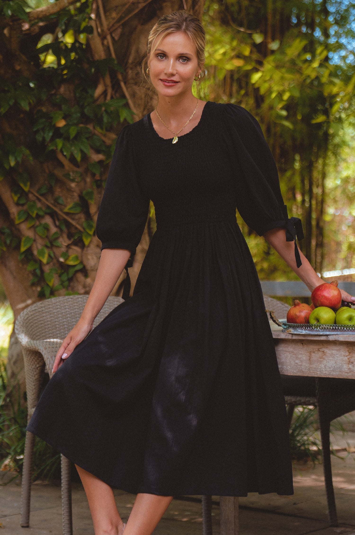 Freya Smocked Linen Midi Dress featuring a smocked bodice and tie up puffy sleeves, styled in a beautiful outdoor setting.