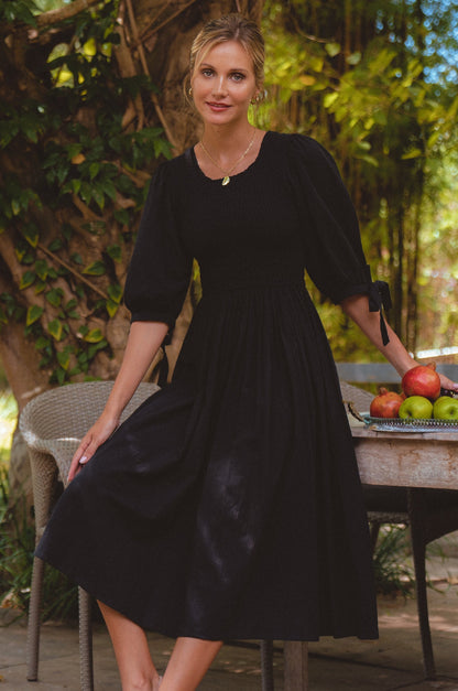 Freya Smocked Linen Midi Dress featuring a smocked bodice and tie up puffy sleeves, styled in a beautiful outdoor setting.