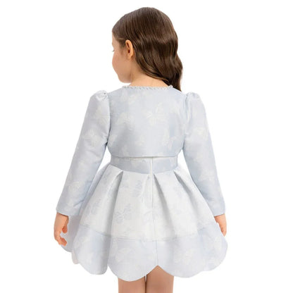 Back view of a little girl wearing a Baby Blue Princess Dress with butterfly patterns and a scalloped hem.