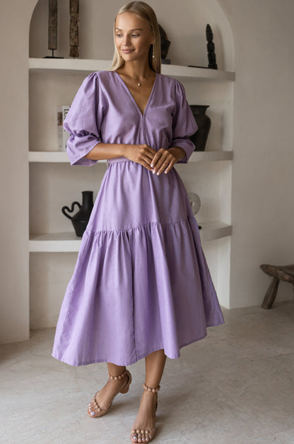 Peony Midi Dress (Sale) model wearing a lavender dress with gathered puff sleeves and a full skirt in a stylish interior.