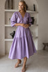 Peony Midi Dress (Sale) model wearing a lavender dress with gathered puff sleeves and a full skirt in a stylish interior.