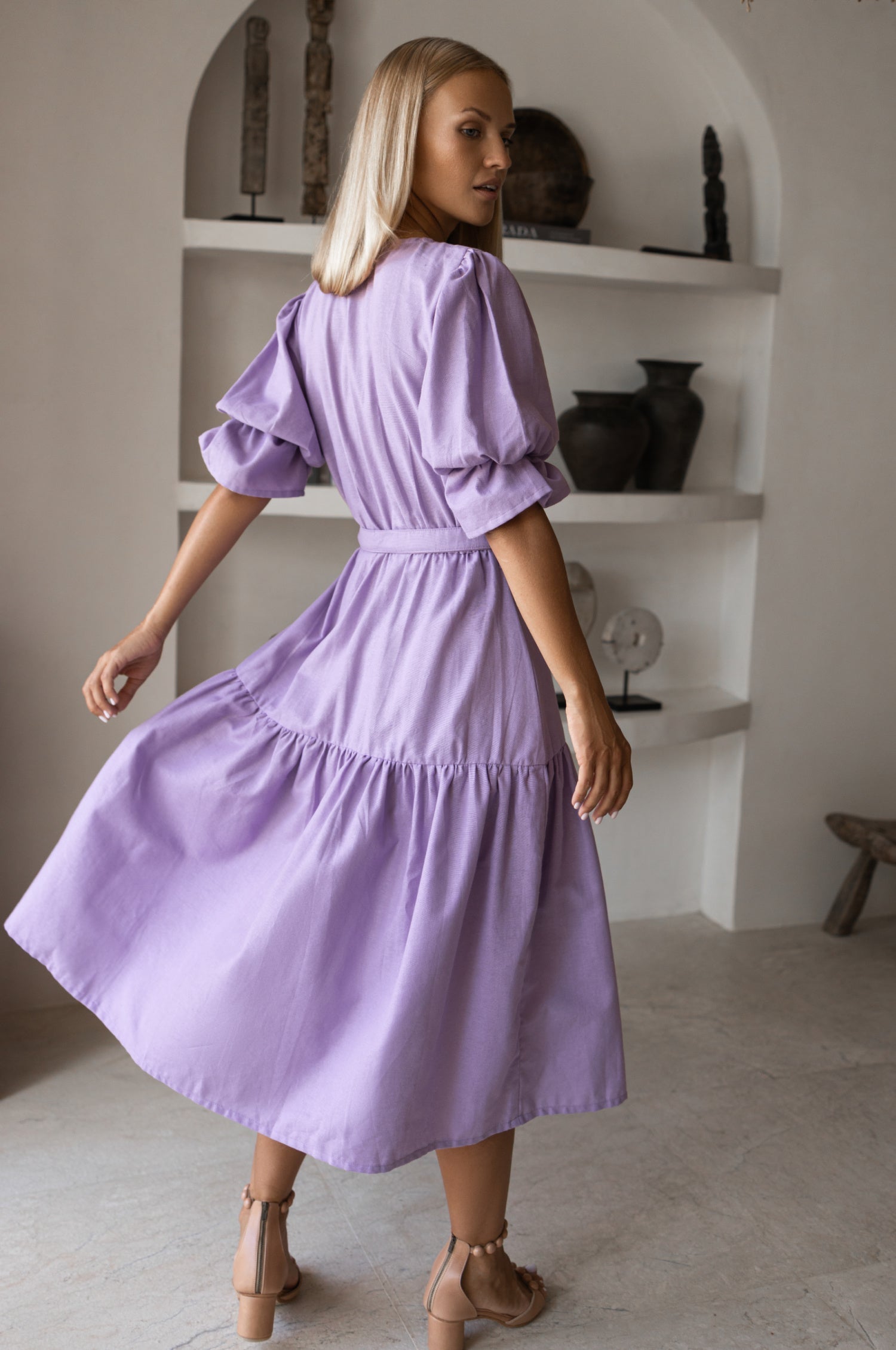 Peony Midi Dress (Sale) - model wearing a lavender midi dress with gathered puff sleeves and matching belt, showcasing back view.