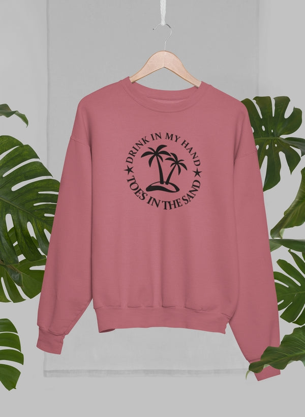 Drink In My Hand Toes In The Sand Sweat Shirt displayed on a hanger with tropical leaves in the background.