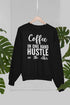 Coffee In One Hand Hustle In The Other Sweat Shirt displayed on a hanger with green plants in the background.