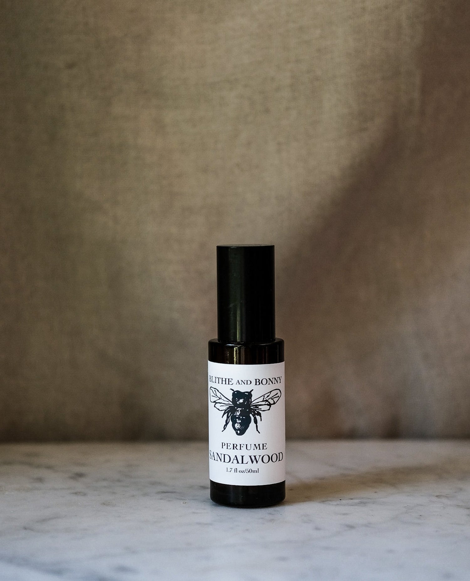 Grand Perfume in a sleek black bottle with sandalwood scent on a marble surface.