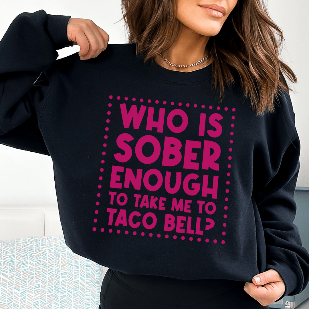 Woman wearing black sweatshirt with pink text: WHO IS SOBER ENOUGH TO TAKE ME TO TACO BELL?